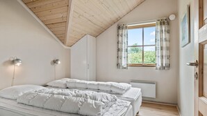 Une chambre avec un plafond en pente, une fenêtre avec des rideaux, un radiateur et une porte.