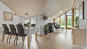 Une cuisine moderne avec un coin repas, un plafond en bois, de grandes fenêtres et une vue sur l’extérieur.