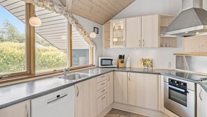 Une cuisine moderne dotée d’une grande fenêtre, d’un plafond en bois, d’appareils électroménagers en acier inoxydable et d’armoires de couleur claire.