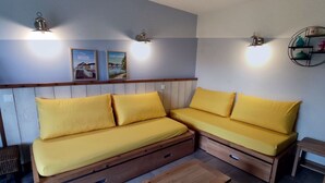 A room with a wooden sofa set with yellow cushions, a wooden coffee table, and wall-mounted light fixtures. - Appartement Belle Dune 2 Chambres (Fort-Mahon Plage)