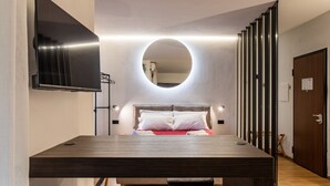 Une chambre à coucher moderne avec un lit, un miroir rond, un téléviseur fixé au mur et un bureau en bois.