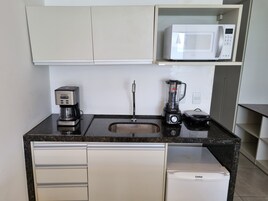 Una kitchenette compacta equipada con cafetera, licuadora, microondas y refrigerador pequeño.