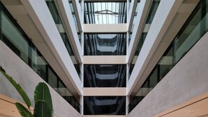 A modern atrium with a central seating area, large potted plants, and a glass ceiling. - Flat Frente Mar R601 (Maceió)