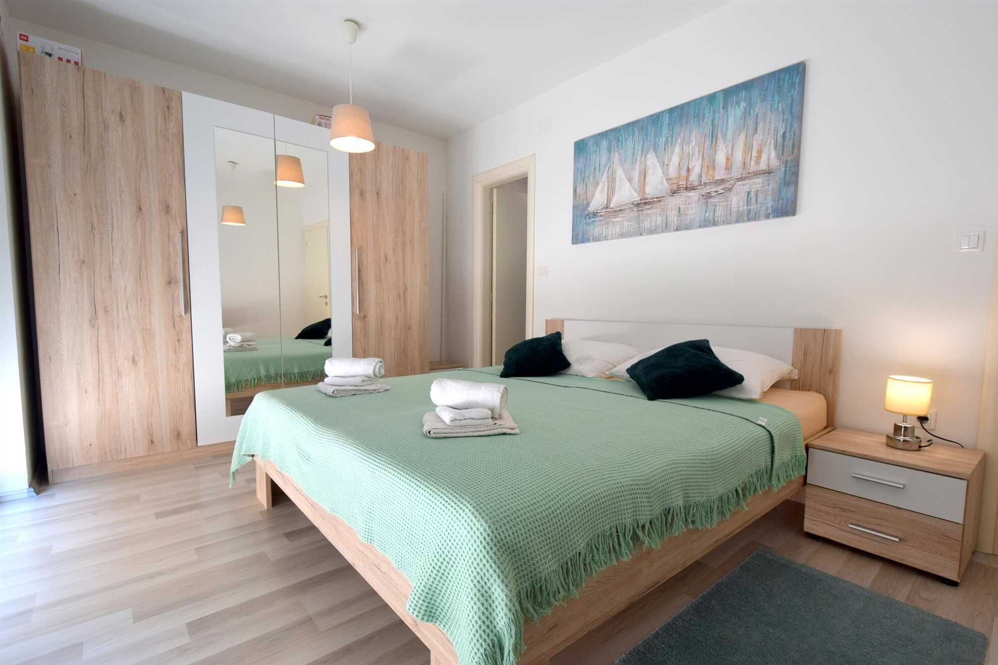 Ein modernes Schlafzimmer mit einem großen Bett, einem Nachttisch, einem Spiegel und einem Gemälde mit Segelbooten.