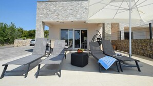 Een moderne buitenruimte met loungestoelen, een tafel, een witte parasol en een stenen muur.