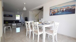 Een eethoek met een witte tafel en stoelen, een schilderij aan de muur en een trap die naar een andere kamer leidt.