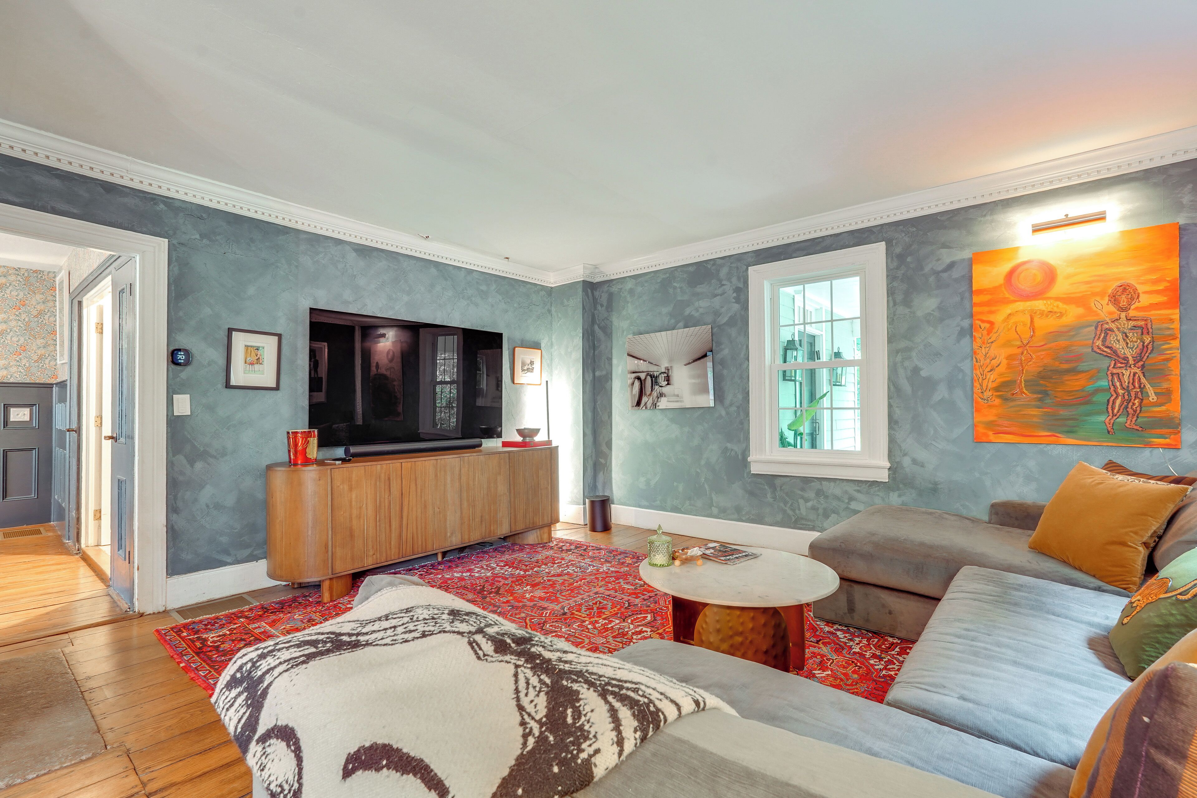 Een woonkamer met een bank, een televisie, een salontafel en een rood, patroonloos tapijt.