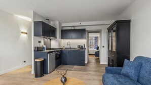 A modern kitchen with dark cabinetry, a dining area with a round table, and a blue sofa. - L’escale 1 - Modern Getaway in the Heart of Honfleur (Honfleur)