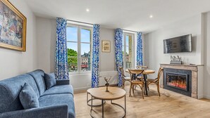 A living room with a sofa, a round table, a fireplace, and a TV mounted on the wall. - L’escale 1 - Modern Getaway in the Heart of Honfleur (Honfleur)