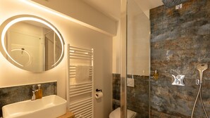 Une salle de bain moderne avec un grand miroir rond, un lavabo blanc, une douche à parois de verre et des toilettes.