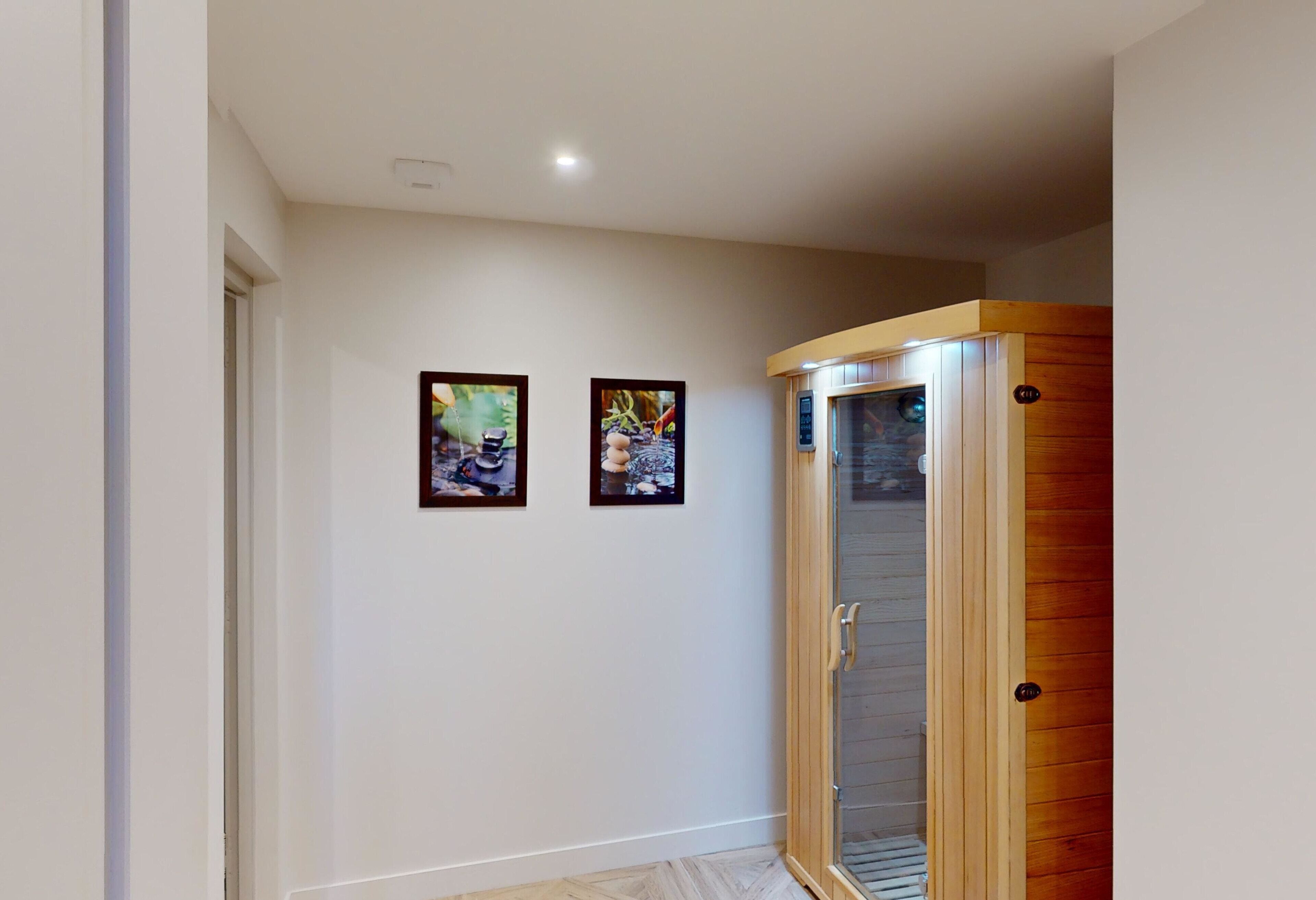 A hallway with two framed pictures on the wall, a wooden door with a glass panel, and a light fixture on the ceiling.