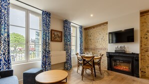 A modern living room with a fireplace, a dining table, and a TV mounted on the wall. - L'Escale du Vieux Port 4P - Closed Garage - Sauna - Air Conditioning (Honfleur)