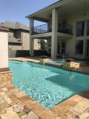 A swimming pool with clear water, surrounded by stone tiles and a covered patio area. - Welcome to 5BR Luxury Home With Pool in beautiful Katy, Texas (Katy)