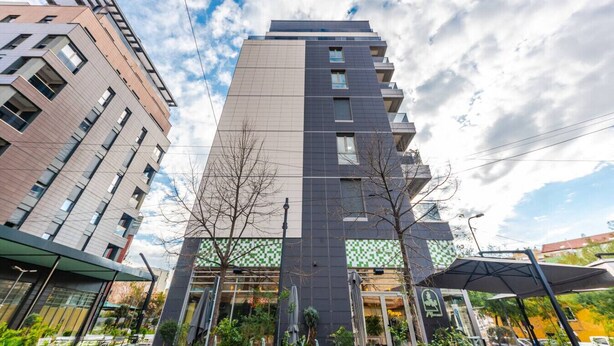 Un moderno edificio de gran altura con varios balcones, ventanas amplias y un diseño de cuadros verdes en la fachada inferior.