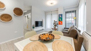 Una sala de estar moderna con un sofá blanco, una mesa de comedor con individuales tejidos, un televisor y una planta.
