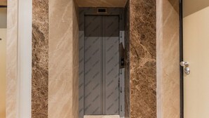 Un elevador moderno con pared de mármol y puerta metálica.