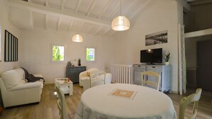 Una sala de estar acogedora con una mesa de comedor redonda, sofás blancos y un televisor.