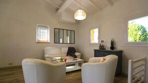 Una sala de estar con un sofá blanco, una mesa de centro y una mesita auxiliar. Hay una ventana con persianas, un espejo y una planta sobre la mesita.
