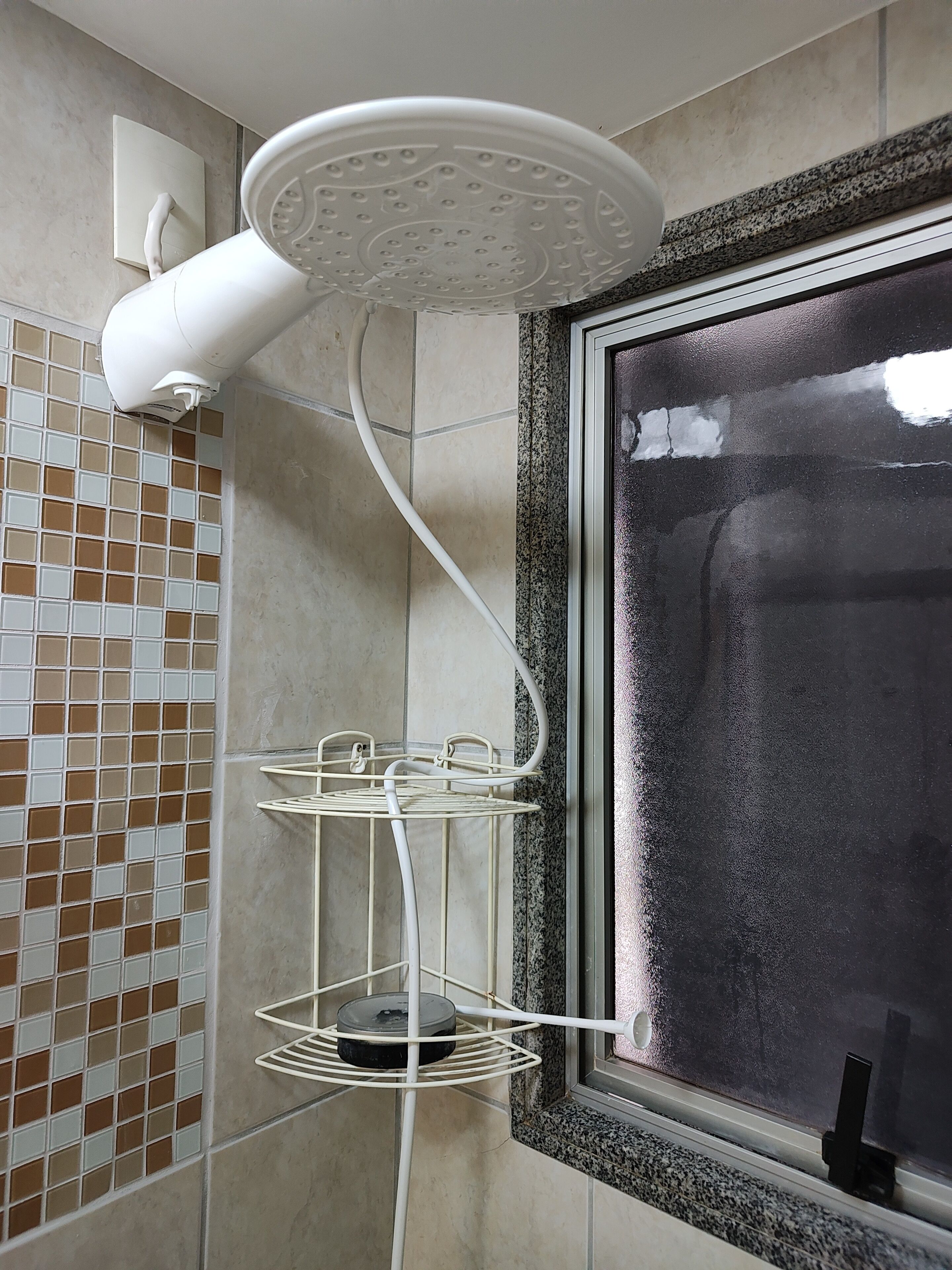 A bathroom with a shower head, a window, and a tiled wall.