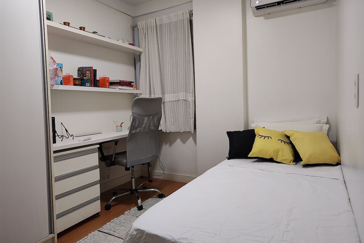 A bedroom with a bed, a desk with a chair, a wardrobe, and a window with curtains.