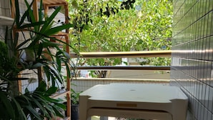 Un balcón con una mesa, plantas en macetas y vistas a un edificio con pared de azulejos.