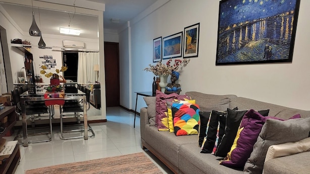 Una sala de estar moderna con un sofá gris, cojines coloridos y un cuadro grande de una escena nocturna.