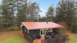 A cabin with a red-tiled roof, a deck with outdoor seating, and a view of a forested area. - 4 bedroom cozy home in Væggerløse (Væggerløse)