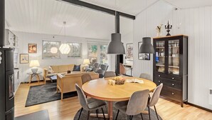 A modern living room with a round wooden dining table, grey upholstered chairs, a beige sofa, and a black cabinet with glass doors. - 4 bedroom cozy home in Væggerløse (Væggerløse)