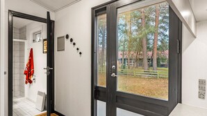 A modern interior with a wooden floor, a black door with a glass panel, and a view of trees and a fence outside. - 4 bedroom cozy home in Væggerløse (Væggerløse)