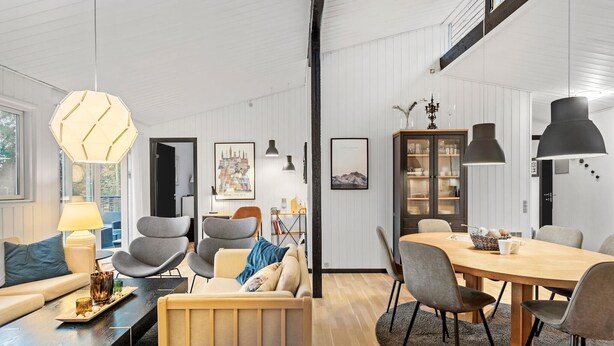A modern living room with a sofa, chairs, a coffee table, and a dining area with a table and chairs. There is a bookshelf and a cabinet with glass doors. - 4 bedroom cozy home in Væggerløse (Væggerløse)