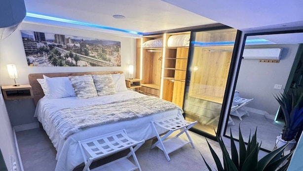 Un dormitorio moderno con una cama grande, un vestidor y vistas a la ciudad a través de un ventanal.