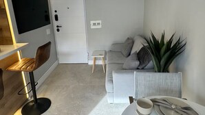 Una sala de estar moderna con un sofá, una mesita con una planta, un televisor montado en la pared y una zona de bar con taburetes.