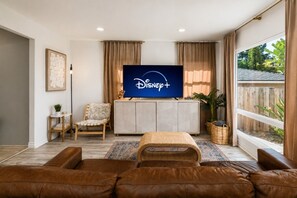 A living room with a flat-screen TV displaying Disney+, a sofa, a chair, a cabinet, and a large window with curtains. - Downtown La Mesa gem (La Mesa)