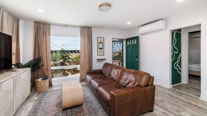 Ein modernes Wohnzimmer mit einer Ledersofa, einem Fernseher und einem Balkon mit Pflanzen.
