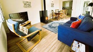 A living room with a sofa, a chair, a TV, a fireplace, and a dining area. - Charming retreat – Near the Sea & Pendine Sands (Pendine)