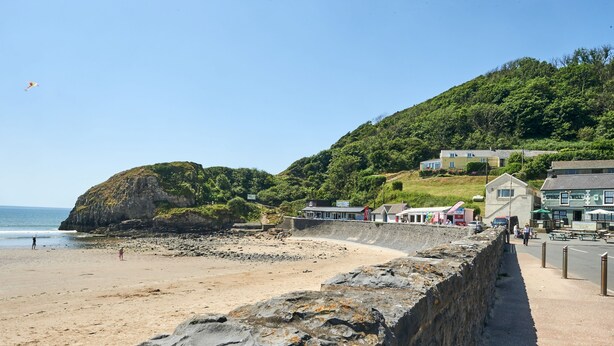 A coastal beach with a stone wall, a small building, and a hill with greenery. - Charming retreat – Near the Sea & Pendine Sands (Pendine)