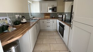 A compact kitchen with white cabinets, a stainless steel sink, a microwave, and a toaster. - Charming retreat – Near the Sea & Pendine Sands (Pendine)
