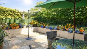 A patio with wicker furniture, a glass table, and a green umbrella. - Charming retreat – Near the Sea & Pendine Sands (Pendine)