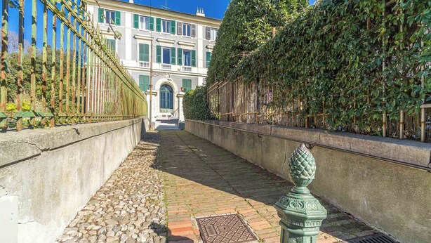 Uma passagem de pedras irregulares leva a um edifício com porta verde e fachada branca.