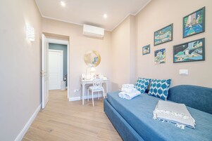 Un dormitorio con cama, escritorio, silla y una pared decorada con cuadros.