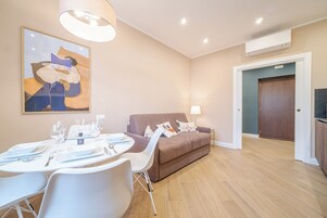 Una sala de estar moderna con una mesa de comedor lista para cuatro personas, un sofá marrón y un cuadro abstracto grande en la pared.
