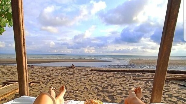 Une scène de plage où l’on voit une personne allongée sur une chaise longue, face à l’océan.