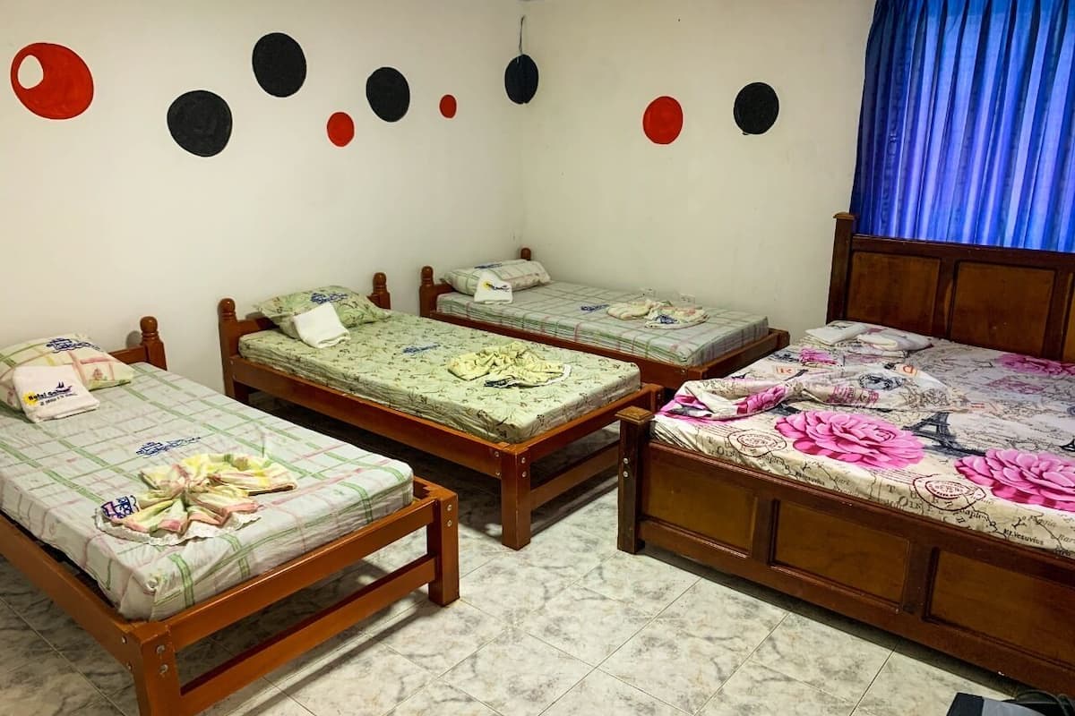 Quarto com três camas de madeira, cada uma com colcha estampada diferente. O chão é de azulejos e a parede possui decorações circulares.