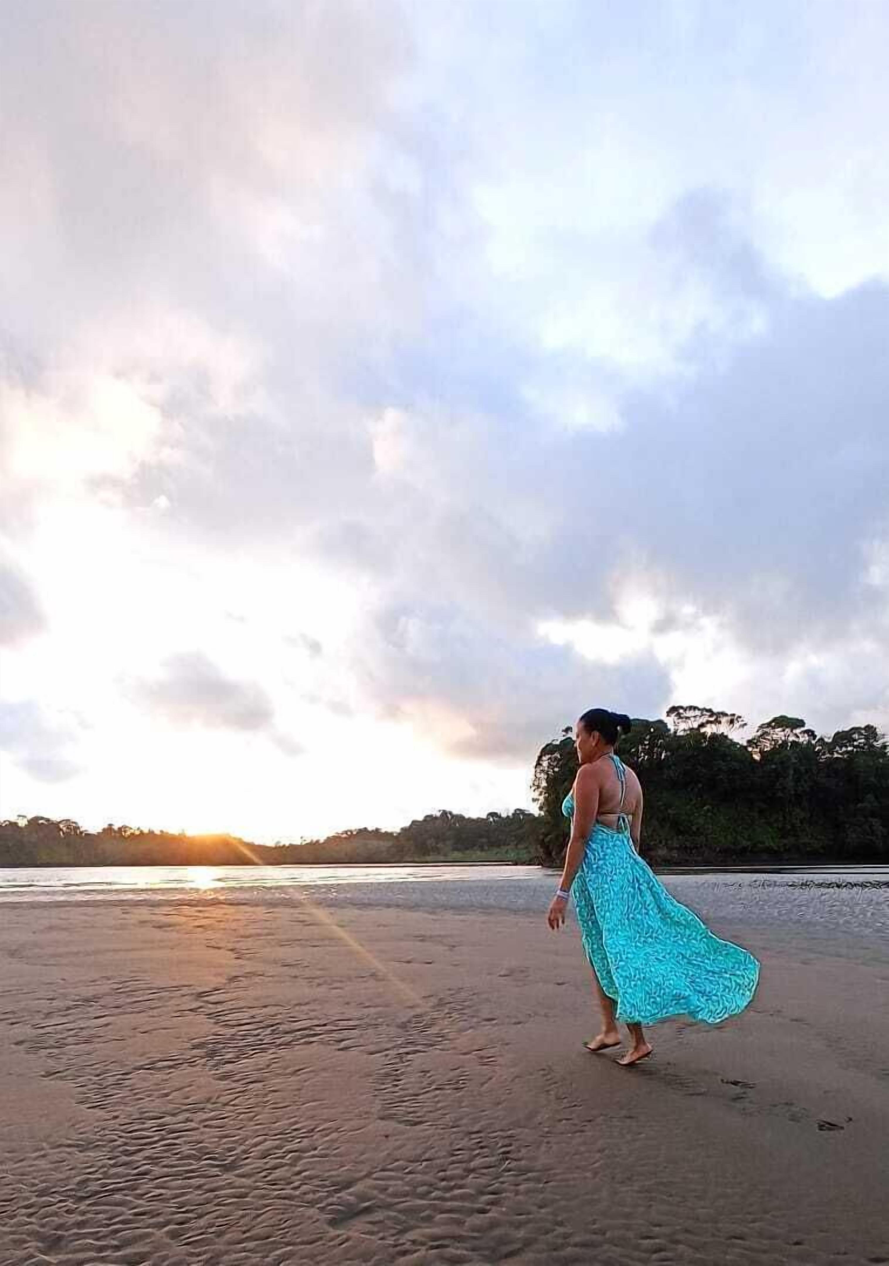 A person walking on a beach with a sunset in the background.