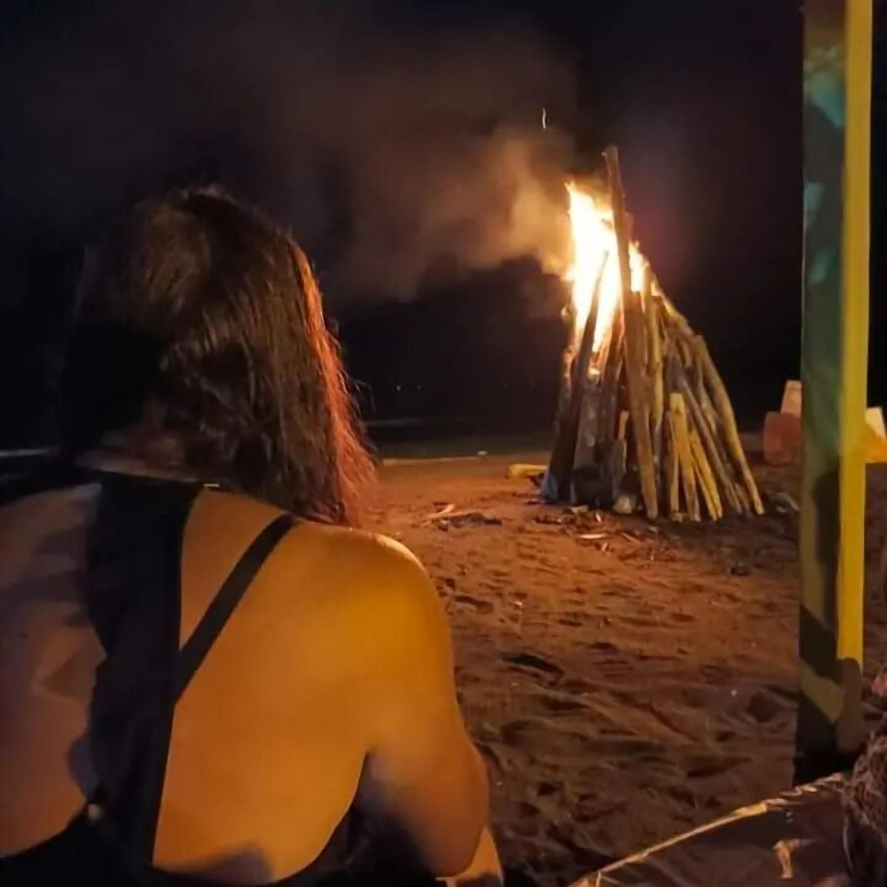 A person sitting on a beach at night, facing a bonfire.