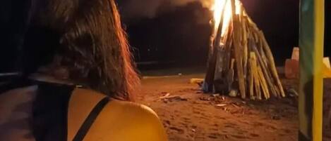 A person sitting on a beach at night, facing a bonfire.