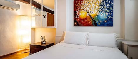 A hotel room with a bed, a bedside lamp, a painting on the wall, and a mirror.