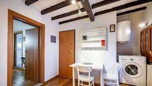A compact room with a wooden floor, a white desk with a chair, a washing machine, and a door leading to another room. - YiD appartamento al Carmine (Firenze)
