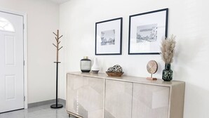 En moderne lobby med et beige konsolbord, to indrammede billeder, en høj gulvlampe og en vase med pampasgræs.