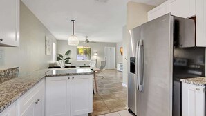 A modern kitchen with white cabinets, a granite countertop, stainless steel appliances, and a dining area with a table and chairs. - Beach Retreat: Walk to Lantana Dining & Shops (Lantana)